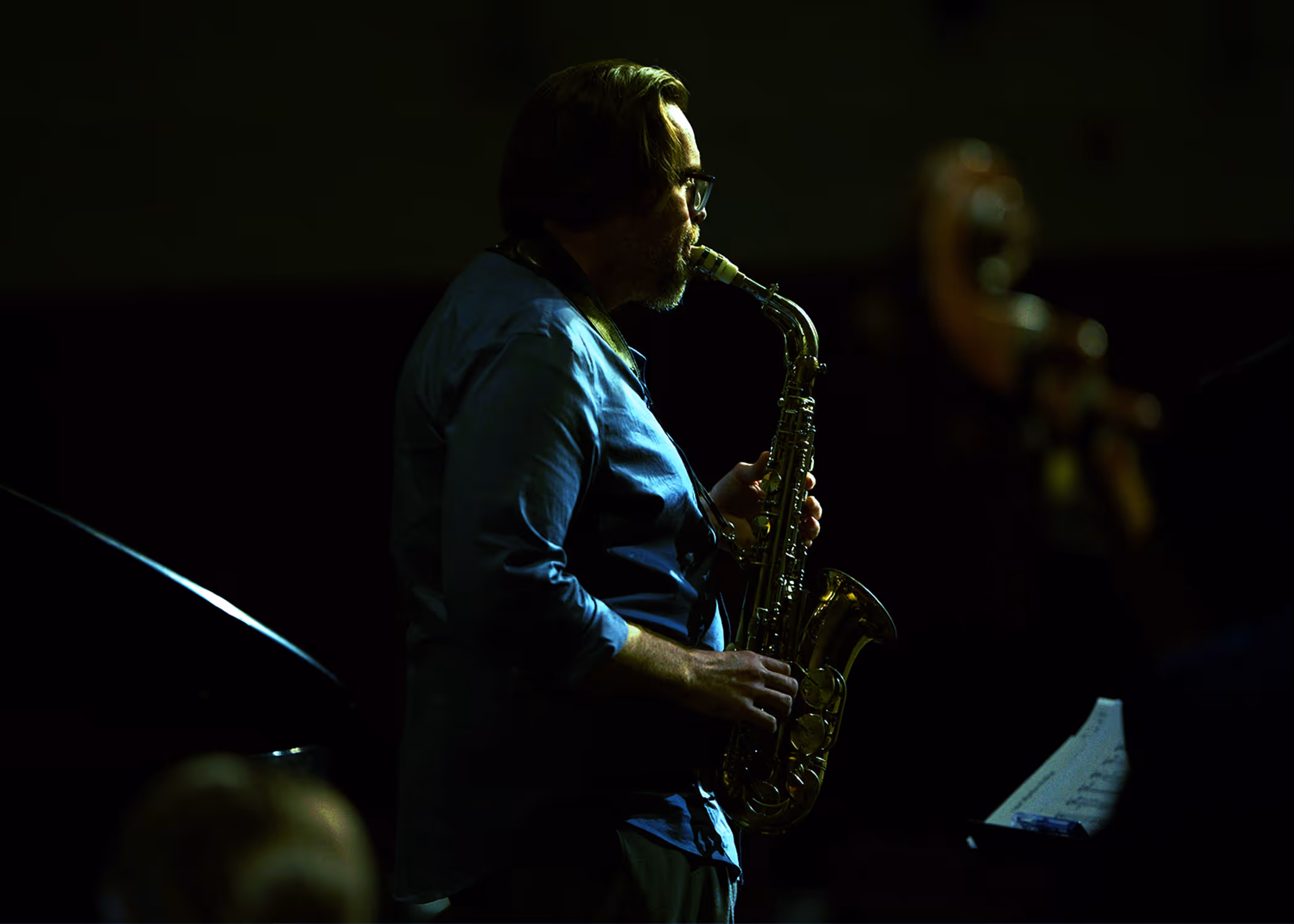 Simon Harding playing saxophone in a pool of stage light